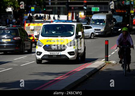 Stockbild eines Polizeiwagens bei einem Notruf, der in der frühen Nachmittagssonne durch den Verkehr auf der Lambeth Palace Road in London, Großbritannien, neben einer Fahrradstraße fährt. Stockfoto