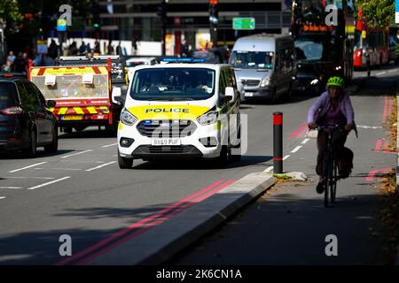 Stockbild eines Polizeiwagens bei einem Notruf, der in der frühen Nachmittagssonne durch den Verkehr auf der Lambeth Palace Road in London, Großbritannien, neben einer Fahrradstraße fährt. Stockfoto