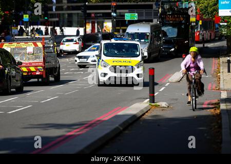 Stockbild eines Polizeiwagens bei einem Notruf, der in der frühen Nachmittagssonne durch den Verkehr auf der Lambeth Palace Road in London, Großbritannien, neben einer Fahrradstraße fährt. Stockfoto