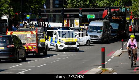 Stockbild eines Polizeiwagens bei einem Notruf, der in der frühen Nachmittagssonne durch den Verkehr auf der Lambeth Palace Road in London, Großbritannien, neben einer Fahrradstraße fährt. Stockfoto