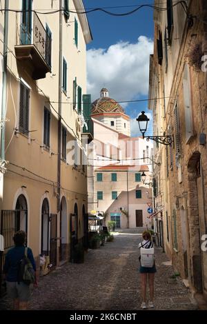 Enge alte Straße mit der bunten gefliesten Kuppel der St. Michael Kirche, Chiesa San Michele in der katalanischen Stadt Alghero Sardinien, Italien Stockfoto