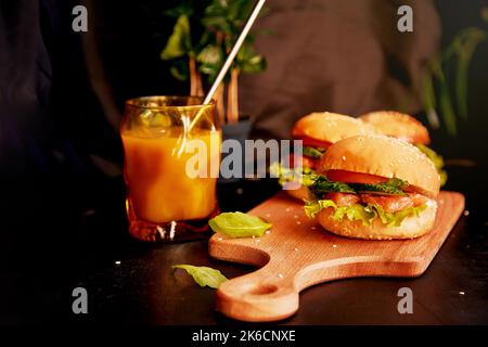 Handgemachte Fischburger mit Kaffee. Gesunde Alternative zu klassischen amerikanischen Hamburgern - Fischburger mit geräuchertem Lachs, Gemüse und Salat. Stockfoto