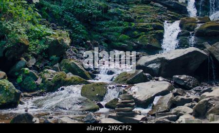 Wasserfall, der die moosigen Steine des Berges wäscht, Spritzer auf die Pflanzen fallen. Gefallene Blätter Rollen den Hügel hinunter, klarer Wasserstrom fließt zwischen den Bergen. Erstaunlich schön der Natur Stockfoto