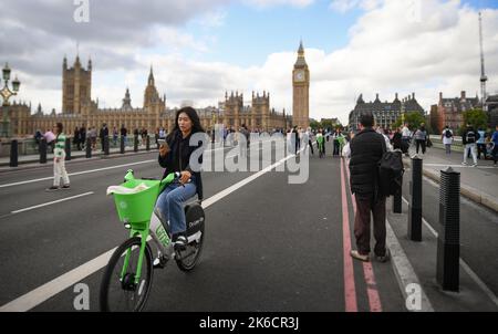 Eine junge Frau schaut auf ein Mobiltelefon, während sie mit einem Lime-Elektrofahrrad über die Westminster Bridge London UK fährt. Stockfoto