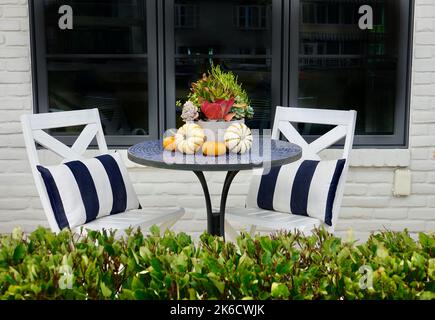 Herbstliche Anordnung von Kürbissen auf einem Bistrotisch mit Stühlen Stockfoto