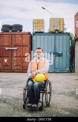 Porträt eines lächelnden Bauarbeiters, der auf der Baustelle im Rollstuhl sitzt Stockfoto