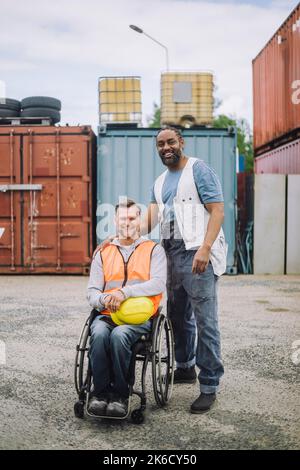 Porträt eines lächelnden Bauarbeiters, der neben einem Kollegen im Rollstuhl auf der Baustelle sitzt Stockfoto