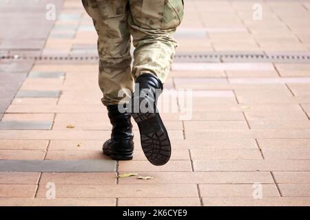 Soldat in militärischer Tarnung und Stiefeln, die die Stadtstraße entlang gehen, Beine auf Bürgersteig. Konzept des Dienstes in der Armee, Mobilisierung Stockfoto