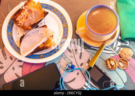 Geröstetes Brot mit Olivenöl und Schinkenscheiben und truthahn zusammen mit Nüssen und elektronischen Geräten Stockfoto