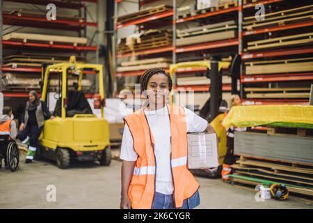 Porträt eines lächelnden Zimmermanns, der einen Karton im Lager trug Stockfoto