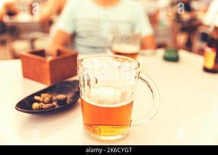 Im Sommer können Sie an einem weißen Tisch in der Terrassenbar ein goldenes Bierglas aus nächster Nähe genießen Stockfoto