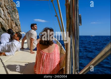 Touristen chillen an Deck eines Charterboots auf dem Weg zu Höhlen entlang der Küste in der Nähe von St. Maria di Leuca und Punta Meliso zu sehen. Apulien (Apulien), Italien. Stockfoto