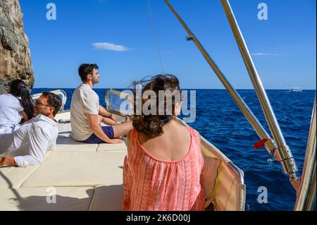 Touristen chillen an Deck eines Charterboots auf dem Weg zu Höhlen entlang der Küste in der Nähe von St. Maria di Leuca und Punta Meliso zu sehen. Apulien (Apulien), Italien. Stockfoto