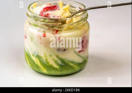 Glas mit Joghurt, Himbeere, weißer Schokolade und Pistazien-Creme mit Löffel auf weißem Hintergrund, Nahaufnahme. Stockfoto
