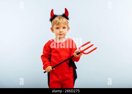 Niedlicher kleiner Junge im Teufel halloween Kostüm mit Hörnern und Dreizack Stockfoto