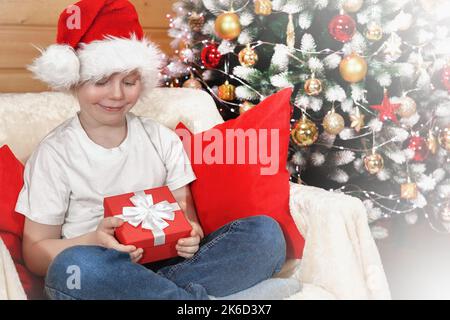 Frohe Weihnachten Kinder. Emotionen eines Kindes. Freudig überrascht Junge in Weihnachtsmann Hut öffnete eine Weihnachts-Box mit einem Geschenk von Santa Claus in der Nähe des Christus Stockfoto