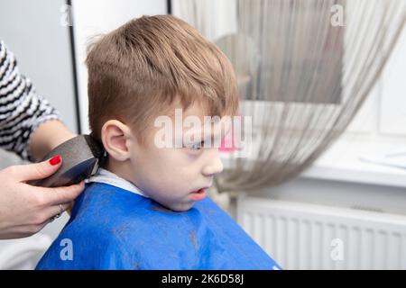 Netter kleiner europäischer Junge, der im Friseurladen Frisur bekommt. Friseur macht eine Frisur für einen Jungen. Stockfoto