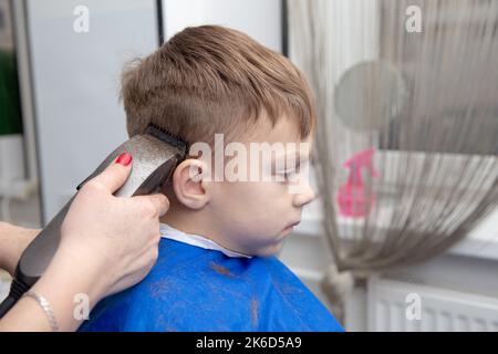 Netter kleiner europäischer Junge, der im Friseurladen Frisur bekommt. Friseur macht eine Frisur für einen Jungen. Stockfoto