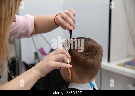 Netter kleiner europäischer Junge, der im Friseurladen Frisur bekommt. Friseur macht eine Frisur für einen Jungen. Stockfoto