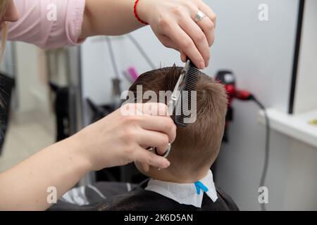 Netter kleiner europäischer Junge, der im Friseurladen Frisur bekommt. Friseur macht eine Frisur für einen Jungen. Stockfoto