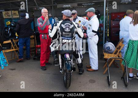 Fahrer Duncan Fitchett oder Jeremy McWilliams sitzen auf einem 1952 Norton-Dayton-Manx mit drei Mechanikern beim Essen von Eis, Goodwood Revival, Chichester, Stockfoto