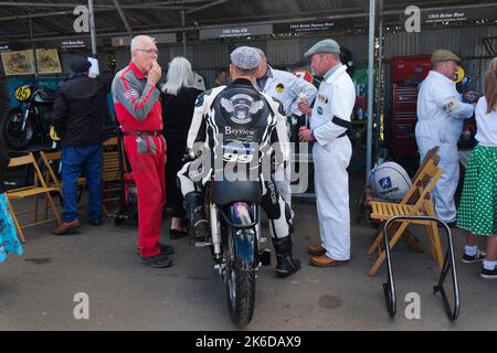 Fahrer Duncan Fitchett oder Jeremy McWilliams sitzen auf einem 1952 Norton-Dayton-Manx mit drei Mechanikern beim Essen von Eis, Goodwood Revival, Chichester, Stockfoto