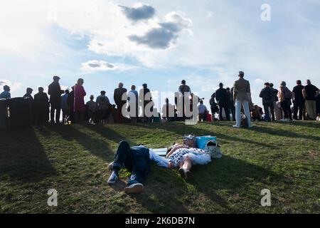 Ein Paar in 1950s-er Kleidung liegt auf dem Grasufer und schläft, während die Zuschauer das Rennen, das BARC Revival Meeting, die Goodwood-Rennstrecke, Großbritannien, beobachten Stockfoto