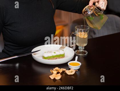 Beschnittene Ansicht einer Frau in schwarzem Rollkragen, die gebrühten grünen Tee ausgießt Stockfoto