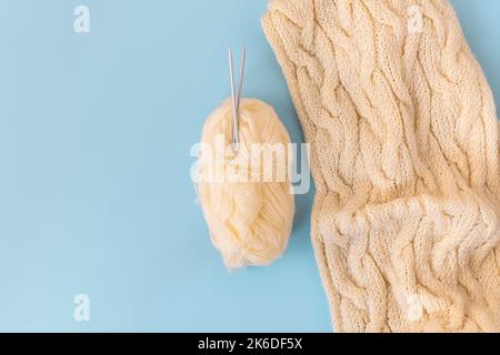 Flaches Lay mit handgearbeitetem Strickschal mit einer Kugel aus Garn und Nadeln auf weichem blauem Hintergrund, Copy Space Stockfoto