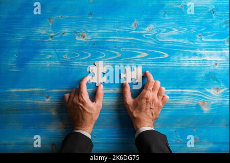 Draufsicht auf die Hände eines Geschäftsmannes, der zwei leere, passende Puzzleteile auf texturiertem blauen Hintergrund hält. Stockfoto