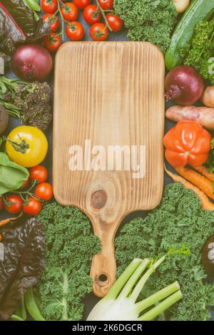 Bio-Gemüse-Sortiment: Brokkoli Blumenkohl Karotten Tomaten Grünkohl pak choy Zwiebeln. Gesunde lokale Bauernprodukte auf dem Tisch, umgeben von Holzhackbrett, Draufsicht, selektiver Fokus Stockfoto