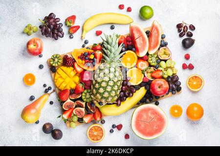 Gesunde rohe Regenbogen Obst Platte Mango Papaya Erdbeeren Orangen Blaubeeren Ananas Wassermelone auf Holzbrett auf weißem Beton Hintergrund, Draufsicht, selektiver Fokus Stockfoto