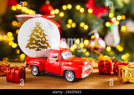 Roter Retro-Spielzeugtruck mit Weihnachtskugel und Geschenkboxen auf Holztisch Stockfoto