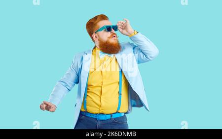 Lustige mollige junge bärtige Mode Kerl in funky Outfit tanzen auf blauem Hintergrund Stockfoto