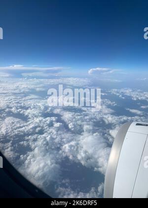 Eine vertikale Aufnahme aus dem Flugzeugfenster mit weißen, flauschigen Wolken am blauen Himmel und dem Motor Stockfoto