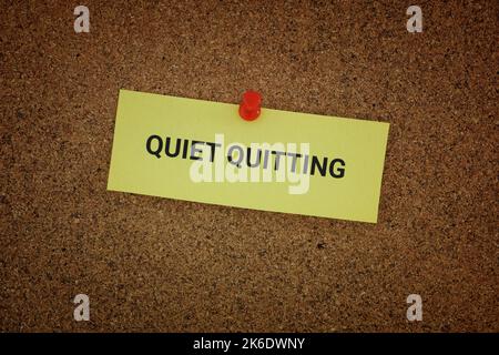 Eine gelbe Papiernote mit den Worten Quiet Quitting darauf, an einem Korkbrett fixiert. Nahaufnahme. Stockfoto