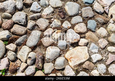 Raues Pflastersteinpflaster auf der Straße als kreative Hintergrundstruktur. Natursteine als Hintergrund. Natürliche große Kopfsteinpflaster mit verschiedenen Größen und Stockfoto