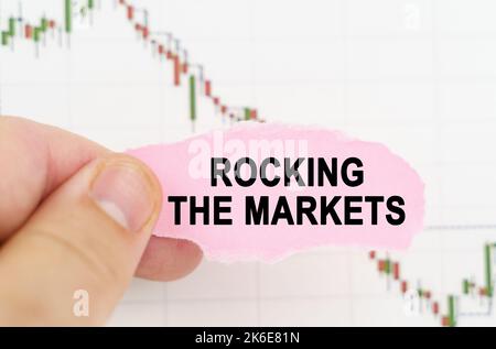 Geschäfts- und Handelskonzept. Vor dem Hintergrund des Zitatdiagramms hält ein Mann ein Schild mit der Aufschrift "Rocking the Markets" Stockfoto