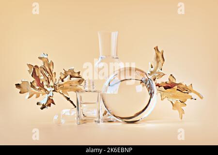 Biophiler Herbsthintergrund. Vergoldete Ahornblätter aus Gold, verzerrt durch transparente Glasgläser, kleine Flaschen. Einfarbig orange beige florale Elemente Stockfoto