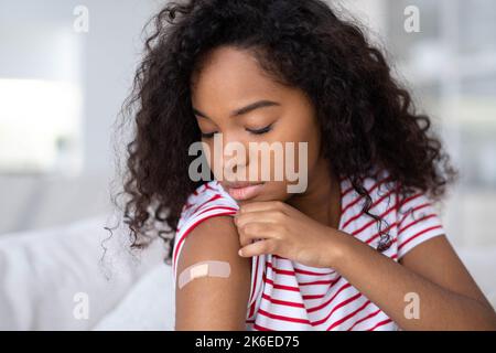 Geimpfte afroamerikanische Frau mit Arm und medizinischem Pflaster Gips auf der Schulter, schwarze Frau nach der Impfdosis gegen Covid Stockfoto