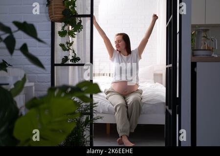 Schwanger glücklich Morgen werdende Mutter aufwachen streicheln ihren Bauch. Frau Hände berühren ihren Bauch, warten Kind, sitzen auf dem Bett Vorbereitung für Stockfoto