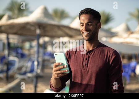 Ein schönes und selbstbewusstes, lächelndes Porträt eines jungen afrikanisch-ägyptischen Mannes, der am Strand ist Stockfoto