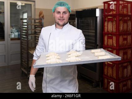 Junger Konditormeister bereitet im Backwarenkochverfahren Croissants zu, bevor er zum Ofen geht Stockfoto