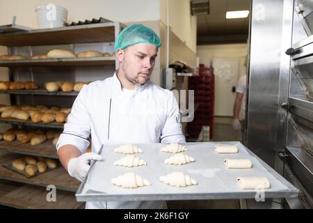 Junger Konditormeister bereitet im Backwarenkochverfahren Croissants zu, bevor er zum Ofen geht Stockfoto