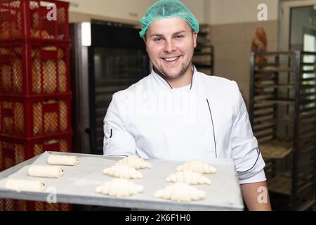 Junger Konditormeister bereitet im Backwarenkochverfahren Croissants zu, bevor er zum Ofen geht Stockfoto