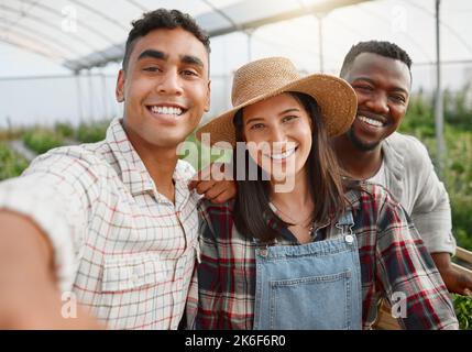 Das Team, das einen so blühenden Garten pflegt. Porträt einer Gruppe von Menschen, die Selfies machen, während sie auf einer Farm zusammenarbeiten. Stockfoto