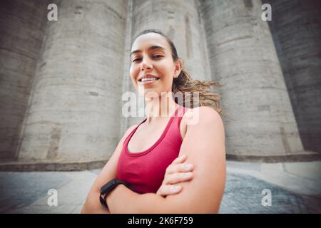 Fitness ist das Leben, das ich wähle. Das verkürzte Porträt einer attraktiven jungen Sportlerin, die beim Laufen im Freien mit gefalteten Armen steht. Stockfoto