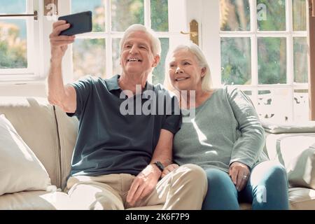 Lächeln. Ein liebevolles Seniorenpaar, das zu Hause in ihrem Wohnzimmer sitzt. Stockfoto