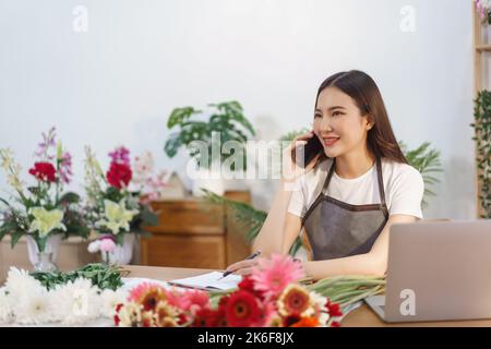 Blumengeschäft Konzept, weibliche Floristin im Gespräch mit dem Kunden auf dem Smartphone und notieren auf Notebook. Stockfoto