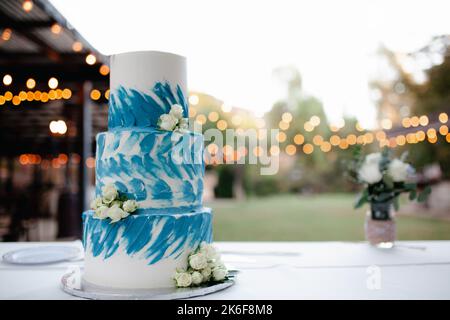 Dreistufige weiße und blaue Hochzeitstorte mit weißen Rosen und Herztopper. Stockfoto